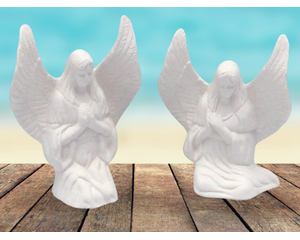 Ready to paint ceramic angel figurines sitting on a rustic table near the ocean.